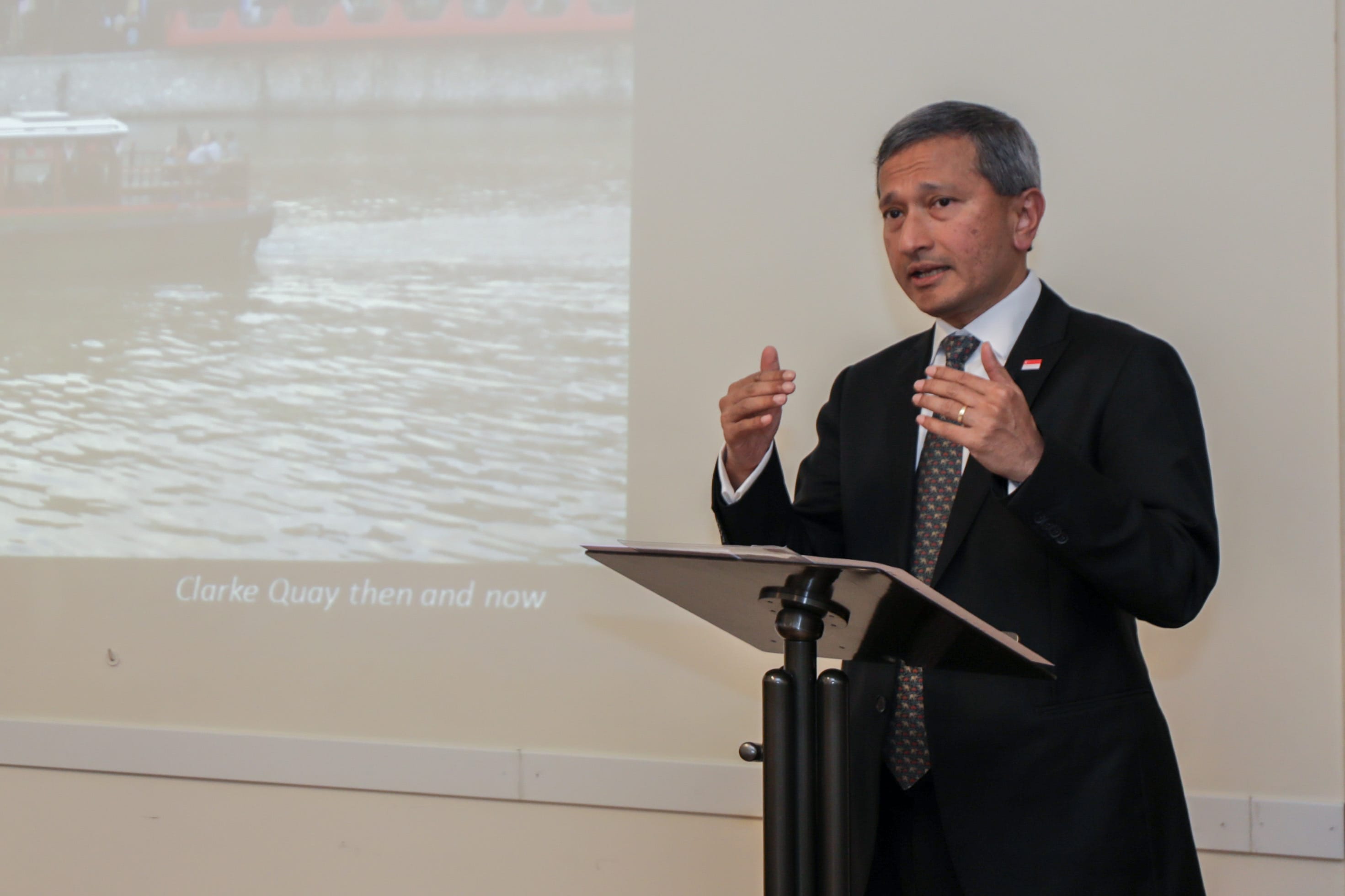 Man in suit gesturing at podium; screen displays "Clarke Quay then and now".
